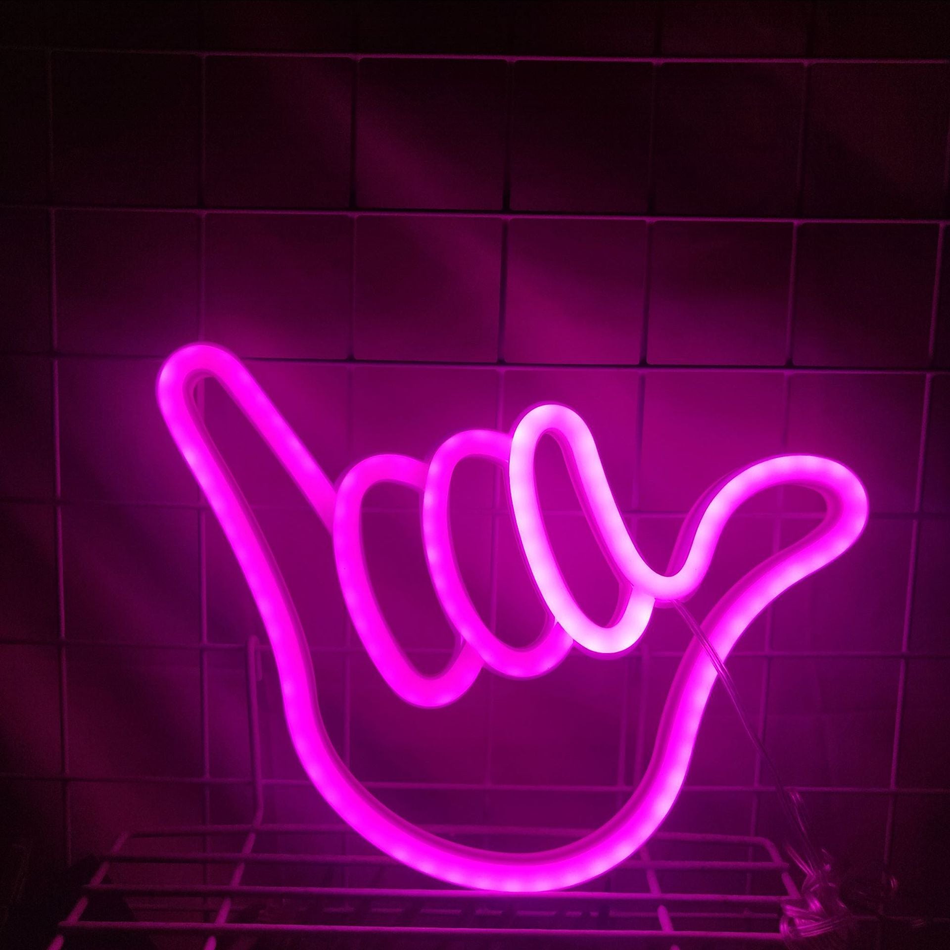 Neon finger sign in pink light on desk near gaming setup